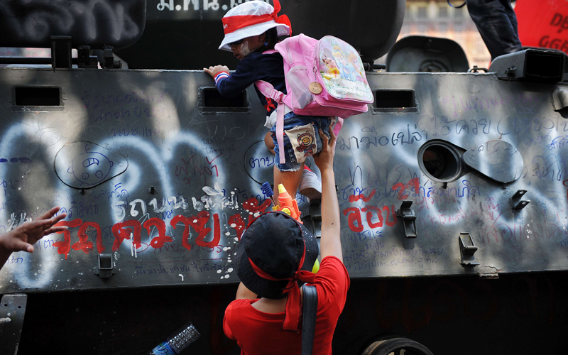 An anti-government 'Red Shirt' protester helps her daughter onto an abandoned army vehicle during celebrations of the Songkran festival marking the Thai new year, at Democracy monument, the re-occupied site of fierce street battles between protesters and the army at the week-end, in Bangkok on April 13.  The Thai authorities will allow "Red Shirt" protesters to keep up their rallies in Bangkok for months if they do not use violence, Deputy Prime Minister Suthep Thaugsuban said. (AFP)