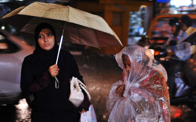 An Indian Muslim woman shelters under an umbrella as an elderly pedestrian drapes herself in plastic to protect against a downpour in Mumbai. (AFP)