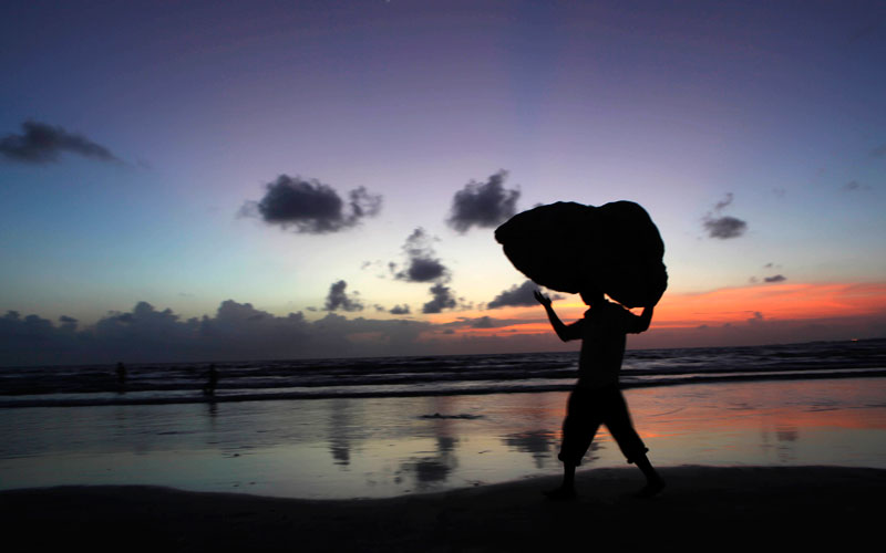 An Indian man carries a sack as he walks along the shores of the Arabian Sea as pre-monsoon clouds hover above Mumbai, India. (AP)