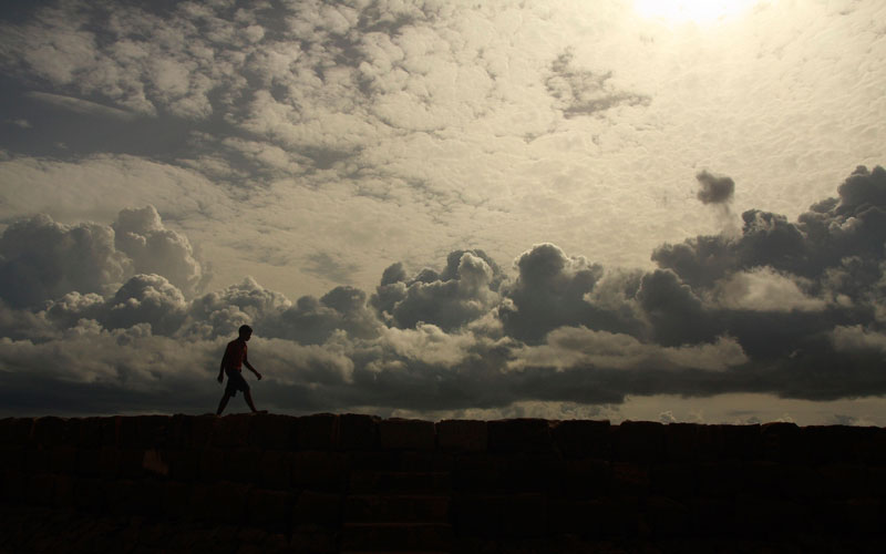 A boy walks along the seawall, against the backdrop of monsoon clouds, on the outskirts of the southern Indian city of Kochi in India. (REUTERS)