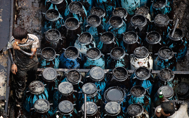 Local fishermen rest near pods of retrieved oil as they clean up the oil, which has spread far from the original explosion site in Xingang port, Dalian, northeastern China. The first details emerged Friday on the cause of China's largest reported oil spill, while environmentalists urged the government to do more to warn local residents of potential danger, saying children are playing still off nearby beaches. (AP)