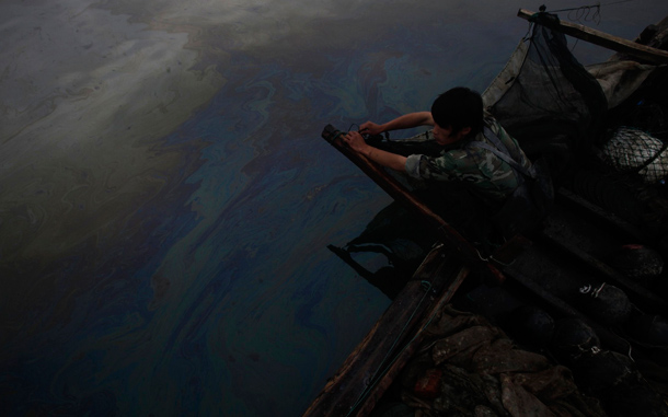 Fisherman works to clean up the oil, which has spread far from the original explosion site in Xingang port, Dalian, northeastern China. The first details emerged on Friday. The cause of China's largest reported oil spill, while environmentalists urged the government to do more to warn local residents of potential danger, saying children are playing still off nearby beaches. (AP)