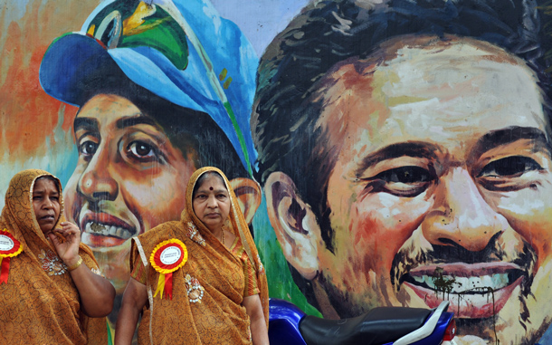 Sari-clad Indian women stand infront of a mural depicting former Indian cricket captain Sourav Ganguly (L) and cricketer Sachin Tendulkar (R) in Bangalore. (AFP)