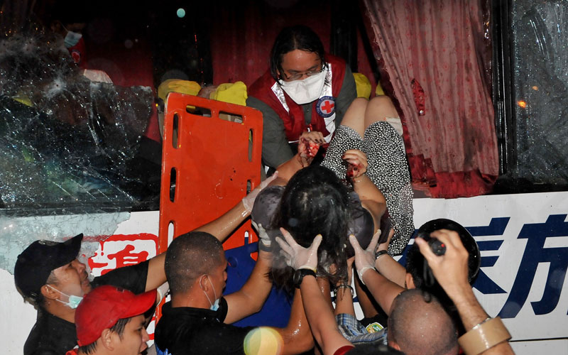 A paramedic (top) lowers one of the wounded survivor from the hijacked bus in Manila. (AFP)