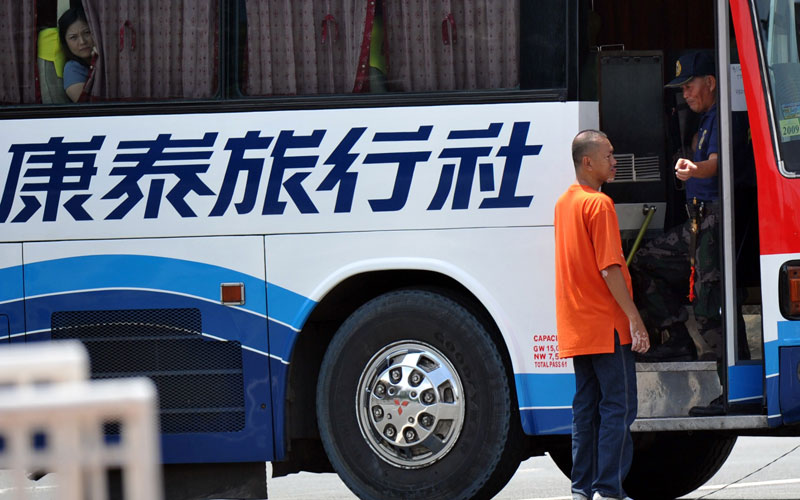 An ex-policeman who hijacked a tourist bus, identified as senior inspector Rolando Mendoza (R-bus entrance), speaks to a negotiator (in orange shirt) while a female hostage (L) peers from the window of the bus in Manila. (AFP)