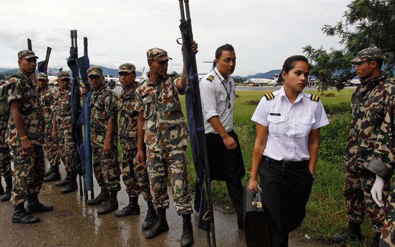 Members of a flight crew walk past Nepalese soldiers waiting with stretchers to carry remains of victims of a plane crash in Katmandu, Nepal. (AP)