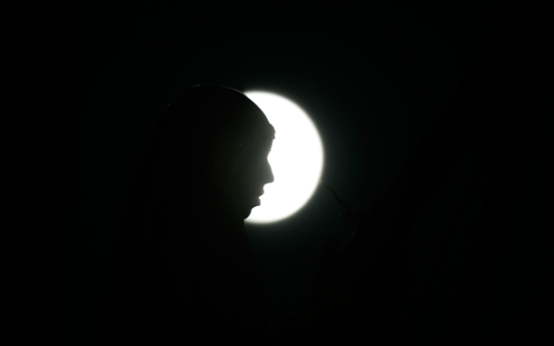 A Palestinian woman reads from the Quran, Islam's Holy book, as the moon shines during the Muslim holy month of Ramadan, in the West Bank city of Nablus. (AP)