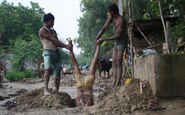 Laborers hold their colleague to install underground electric cables on a roadside at Noida in the northern Indian state of Uttar Pradesh. (REUTERS)