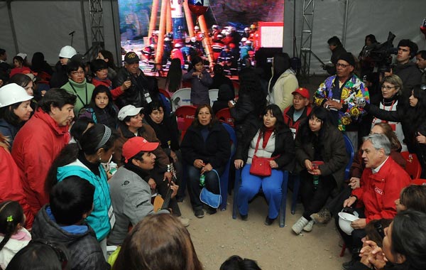 In this photo released by the Chilean presidential press office, Chile's President Sebastian Pinera, sitting bottom right holding hard hat, and his Mining Minister Laurence Golborne, second from left in red jacket, meet with relatives of the 33 trapped miners at the San Jose mine near Copiapo, Chile. (AP)