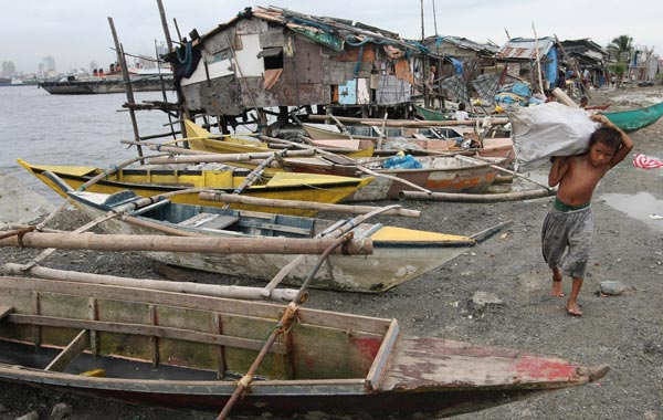 A Filipino boy carries a sack of firewood while walking past docked fishing boats at a coastal fishing community in Manila, Philippines. (EPA)