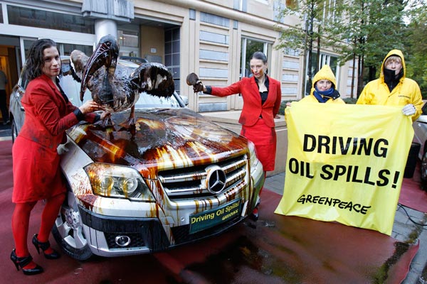 Members of environmental group Greenpeace pose around a luxury car covered by oil, outside the European carmakers association ACEA office in Brussels. (REUTERS)