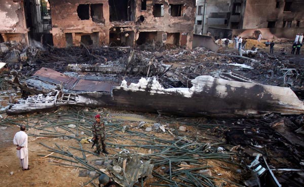 A soldier stands guard in front of the wreckage of an airplane which crashed in Karachi. A plane carrying eight people crashed early on Sunday in a residential area of Karachi, Pakistan's biggest city, setting buildings on fire. (REUTERS)