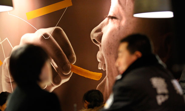 A policeman (R) and customers sit in front of a giant advertising board during the opening ceremony of a newly-renovated McDonald's restaurant to mark the 20th anniversary of McDonald's in China, in Beijing. McDonald's Corp plans to increase its investment in China by 40 percent in 2011, primarily by opening 175-200 new restaurants in the country, the company said in a statement. (REUTERS)