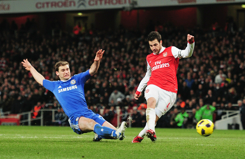 Cesc Fabregas scores Arsenal’s second goal despite a challenge by Branislav Ivanovic of Chelsea during the Premier League match at the Emirates Stadium in London on Monday. (GETTY)