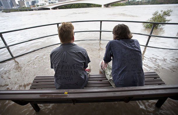 Two people sit on a bench surrounded by water to look at the swollen Brisbane river after floodwaters peaked early morning in Brisbane. Australia's third-largest city Brisbane was turned into a "war zone" on January 13 with whole suburbs under water and infrastructure smashed as the worst flood in decades hit 30,000 properties. (AFP)