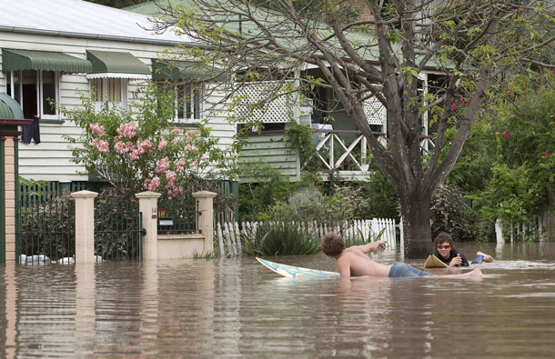 Two young men paddle their surf boards through the floodwaters of West End despite the risks after floodwaters peaked early morning in Brisbane. Australia's third-largest city Brisbane was turned into a "war zone" on January 13 with whole suburbs under water and infrastructure smashed as the worst flood in decades hit 30,000 properties. (AFP)