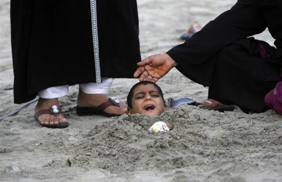 A woman places her hand on her son's head as he lies buried in sand up to his neck during a partial solar eclipse at Karachi's Clifton beach. Yasir, a seven-year-old handicapped boy, joined people with disabilities who were buried chest-deep during the partial solar eclipse on Tuesday, as part of a traditional superstition that it would bring healing to their bodies. (REUTERS)