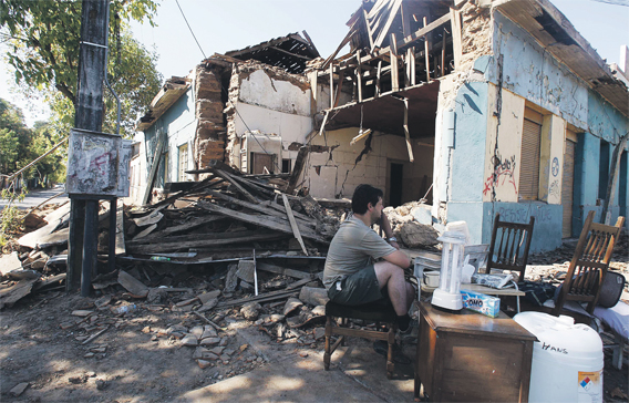 A man sitting with his belongings outside his home in Talca, Chile. (REUTERS)