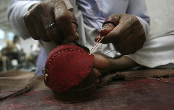 A worker stitches two leather halves together as part of the cricket ball making process at a factory in Meerut, 80 km (50 miles) northeast of Delhi. (REUTERS)