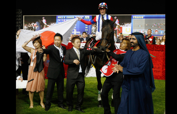 Mirco Demuro (top), riding Victoire Pisa, holds the flag of Japan as Vice President and Prime Minister of the UAE and Dubai's ruler, His Highness Sheikh Mohammed bin Rashid Al Maktoum (R) applauds, after Demuro won the eighth and final race of the 16th Dubai World Cup at the Meydan Racecourse in Dubai. (REUTERS)