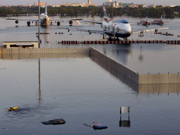 A man swims with an inflatable raft behind a fence near a plane sitting on the flooded tarmack of the closed Don Muang airport November 3, 2011 in Bangkok,Thailand. (GETTY)